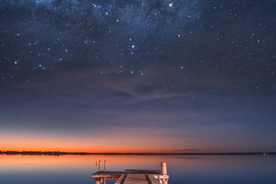 A pier leading out to the water overlooking the night sky full of stars for stargazing in Avon, NC.